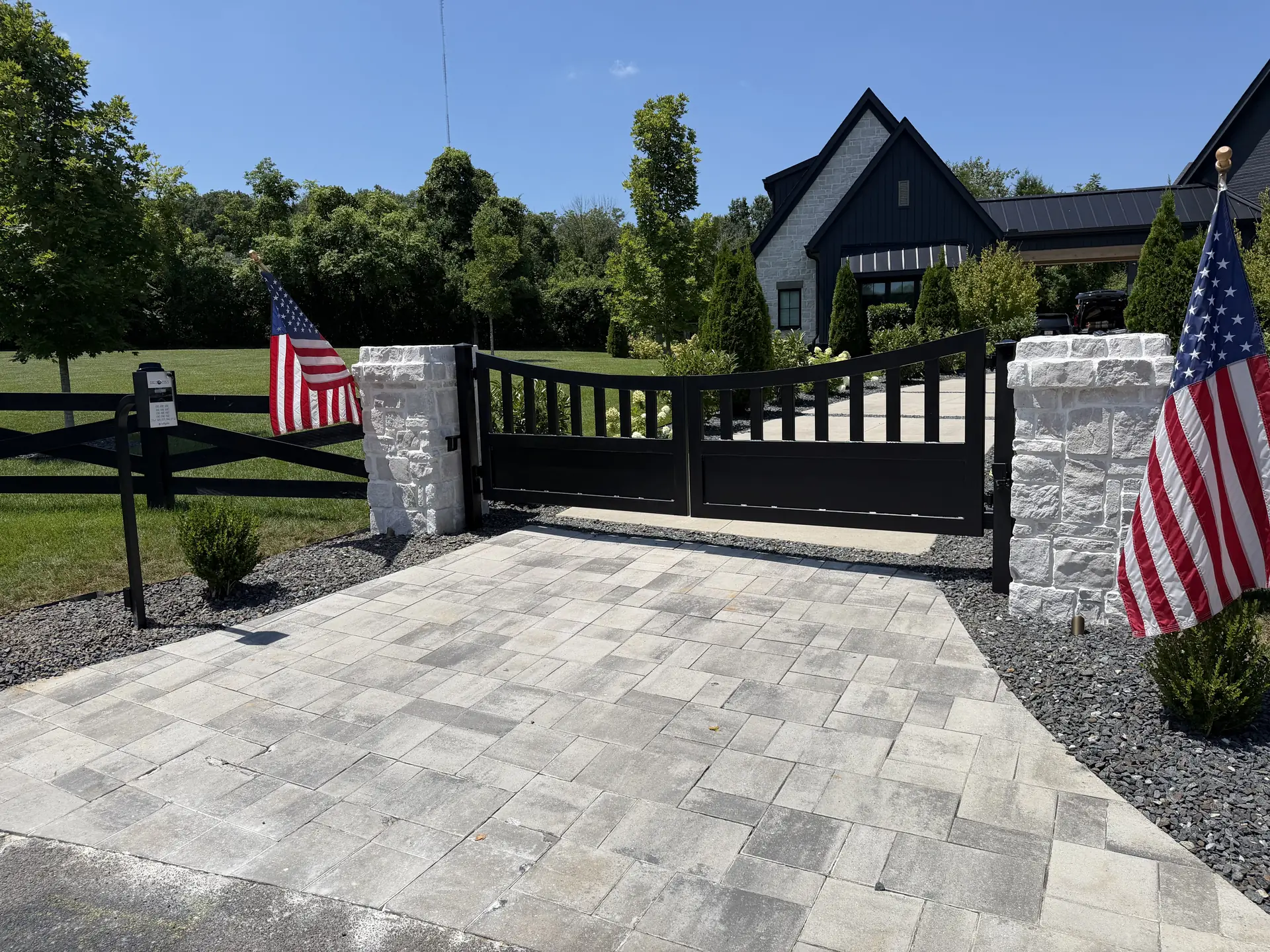 Black automatic gate with stone columns and American flags at a Nashville property